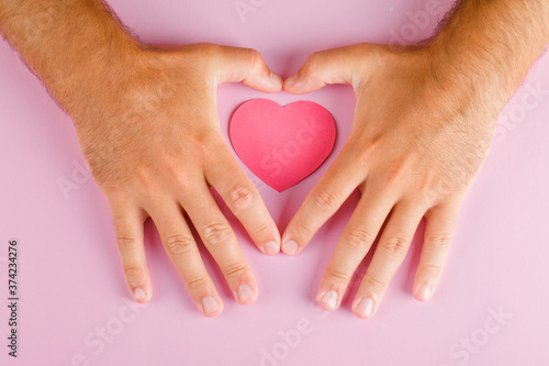 Relationship concept on pink background flat lay. hands protecting paper cut heart.