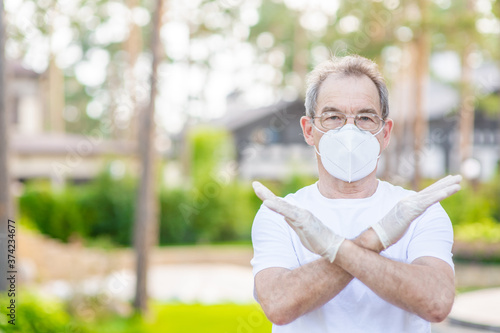 Senior man wearing eyeglasses and protective mask shows stop sign. Empty space for text