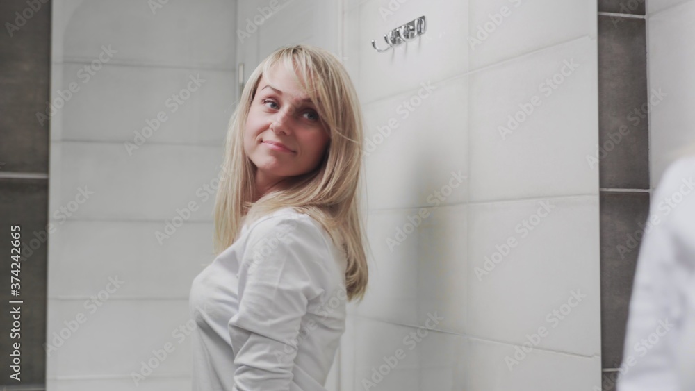 Elegant young woman looking at mirror in bathroom Elegant young woman looking at mirror in bathroom