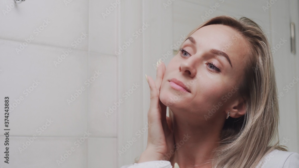 Woman applying cream under the eyes and looking in mirror enjoy natural beauty and healthy Woman applying cream under the eyes and looking in mirror enjoy natural beauty and healthy