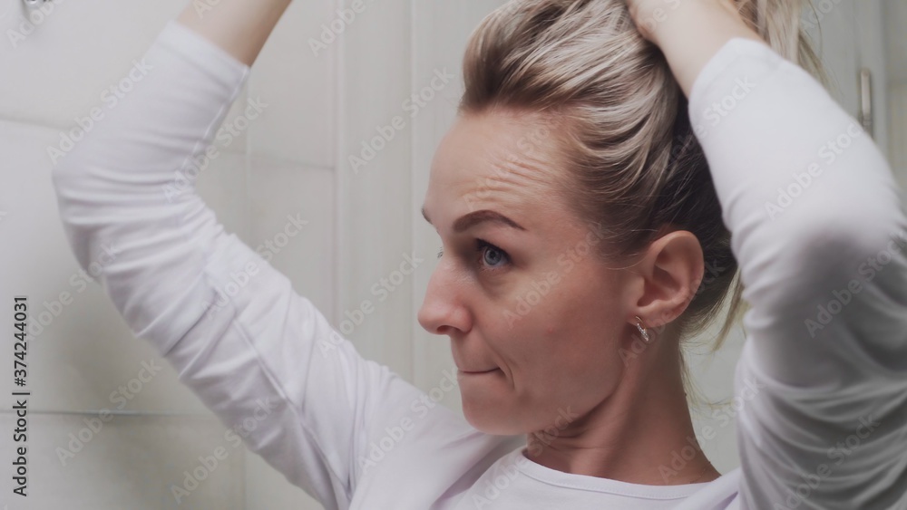 A young woman tucks her hair into an elastic band and look at the mirror A young woman tucks her hair into an elastic band and look at the mirror