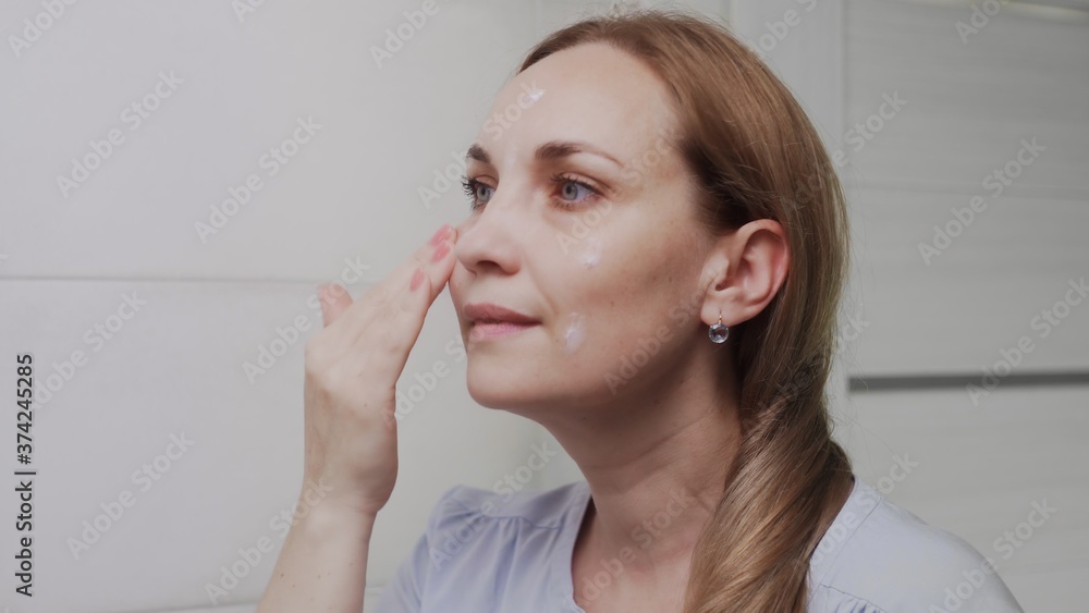 Adult woman applying cream and looking in mirror enjoy natural beauty and healthy Adult woman applying cream and looking in mirror enjoy natural beauty and healthy