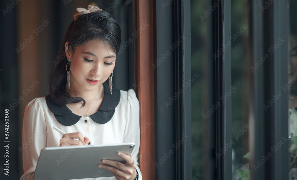 Young asian businesswoman working with tablet while standing nera the window glass in modern office.