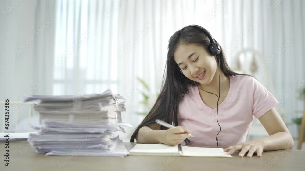 Young Asian woman wears pink shirt and black headset conference calling on laptop talks with online teacher studying, working from home. Lady student e learning using computer webcam Young Asian woman wears pink shirt and black headset conference calling on laptop talks with online teacher studying, working from home. Lady student e learning using computer webcam
