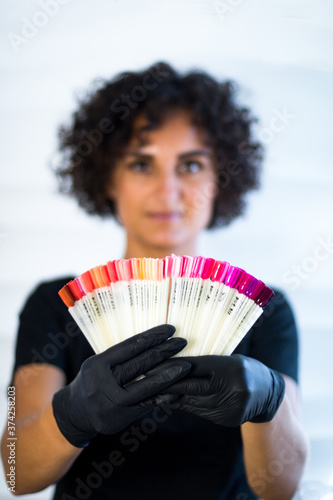 manicurist master in black gloves is holding samples of nail tips on the foreground. blured face