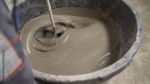 Mix the solution with a self-leveling floor in a bucket. The worker mixes the solution in a bucket using a mixer. Mixing plaster solution in a bucket using electric drill. Construction and renovation 