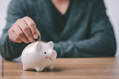 business finance saving and investment concept. hand put money coin into piggy bank for saving money wealth.