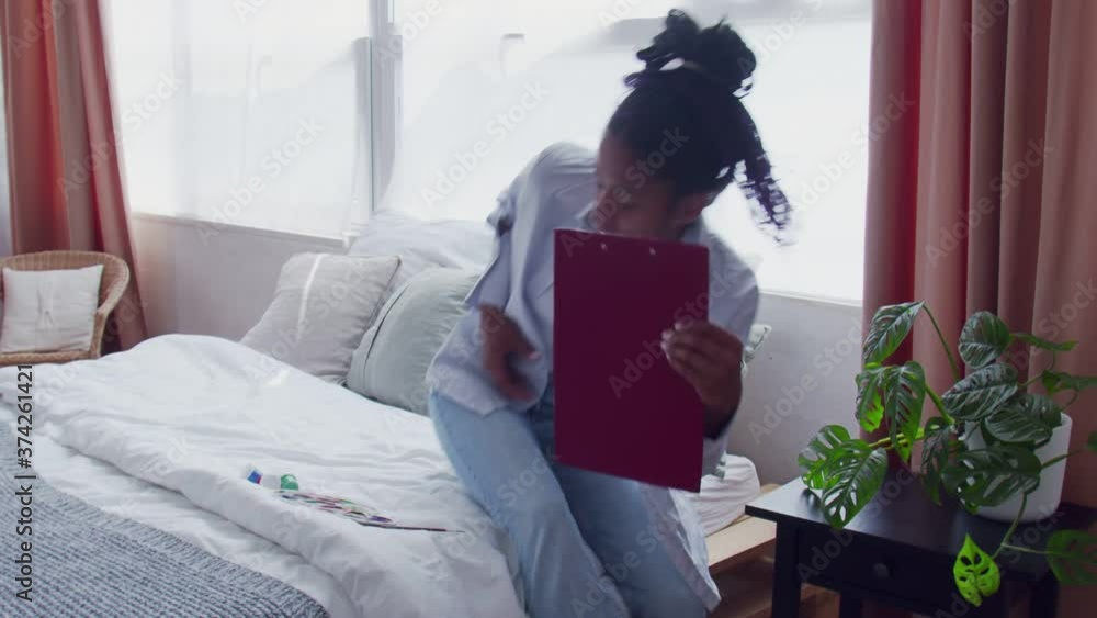Young African American woman sitting in bed and painting picture