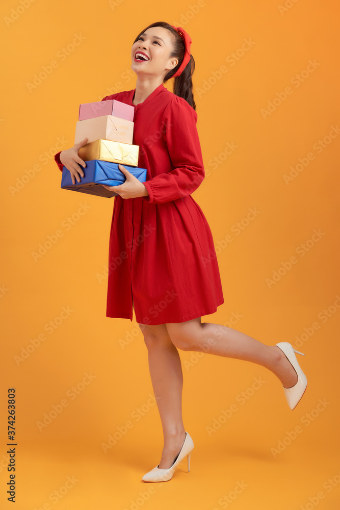 Happy young Asian woman holding stock of gift boxes over orange background. Happy young Asian woman holding stock of gift boxes over orange background.
