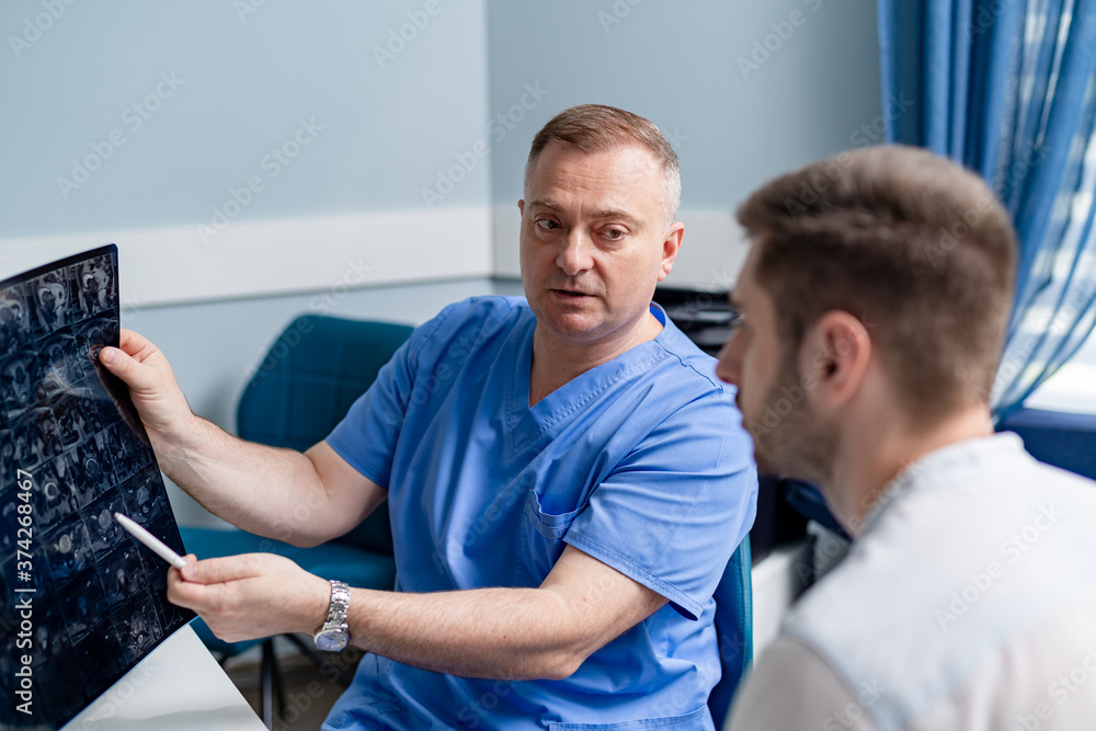 Doctor examining x-ray of a patient. Male radiologist sitting at table. Medical office background. Doctor examining x-ray of a patient. Male radiologist sitting at table. Medical office background.