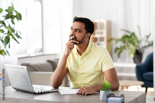 remote job, technology and people concept - young indian man with notebook and laptop computer at home office