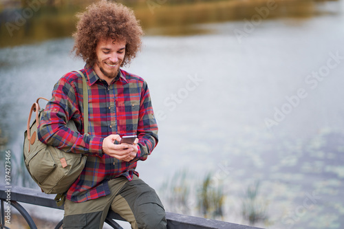 Young handsome man with curly hair using smartphone in ppark. photo