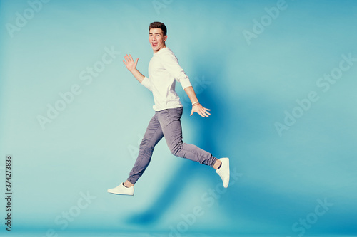 Colorful studio portrait of happy young man dancing jumping against blue background.