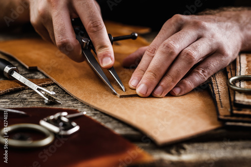 Close up of a shoemaker or artisan worker hands. Leather craft tools on old wood table. Leather craft workshop.
