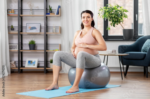 pregnancy, sport and people concept - happy pregnant woman exercising on fitness ball at home