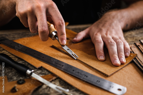 Close up of a shoemaker or artisan worker hands. Leather craft tools on old wood table. Leather craft workshop.