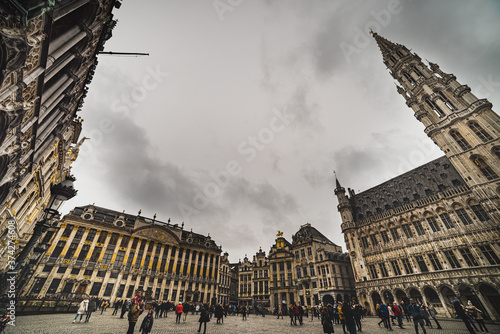 People in the historical Grand Place with the City Hall tower rising in the scene. People walk on the cobbled Grand Square amid Gothic and Baroque architecture - Brussels, Belgium