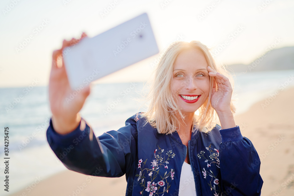 Young smiling woman taking selfie by smartphone at the sea shore.