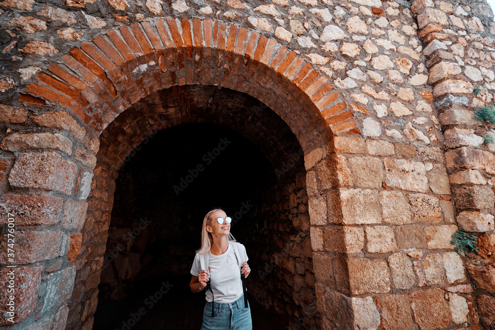 Young traveling woman with rucksack walking in ancient fortress.