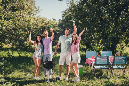 Hello summer. Full length photo of positive girls guys best fellows enjoy vacation weekend rest relax outdoors cook grill meat sausages raise beer bottle under green tree