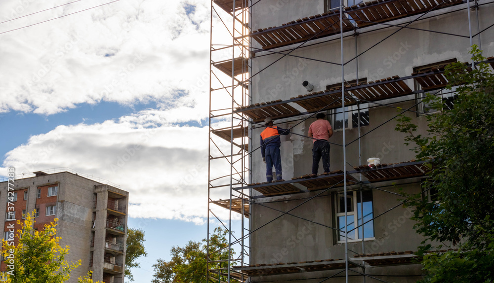Scaffolding that provides sites for unfinished work on a new apartment building.Workers paint the walls