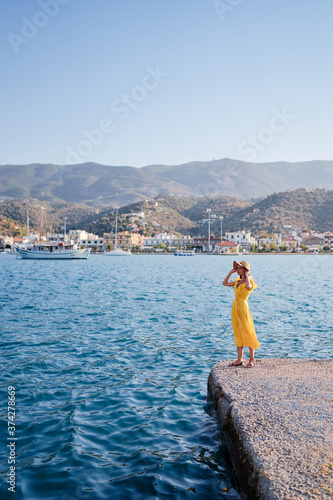 Traveling by Greece. Young happy woman enjoying the view of Poros bay on the sea promenade.