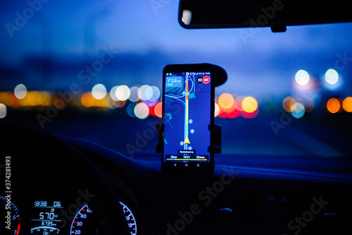 Smartphone with map on the screen in car. Automobile dashboard in night mode.