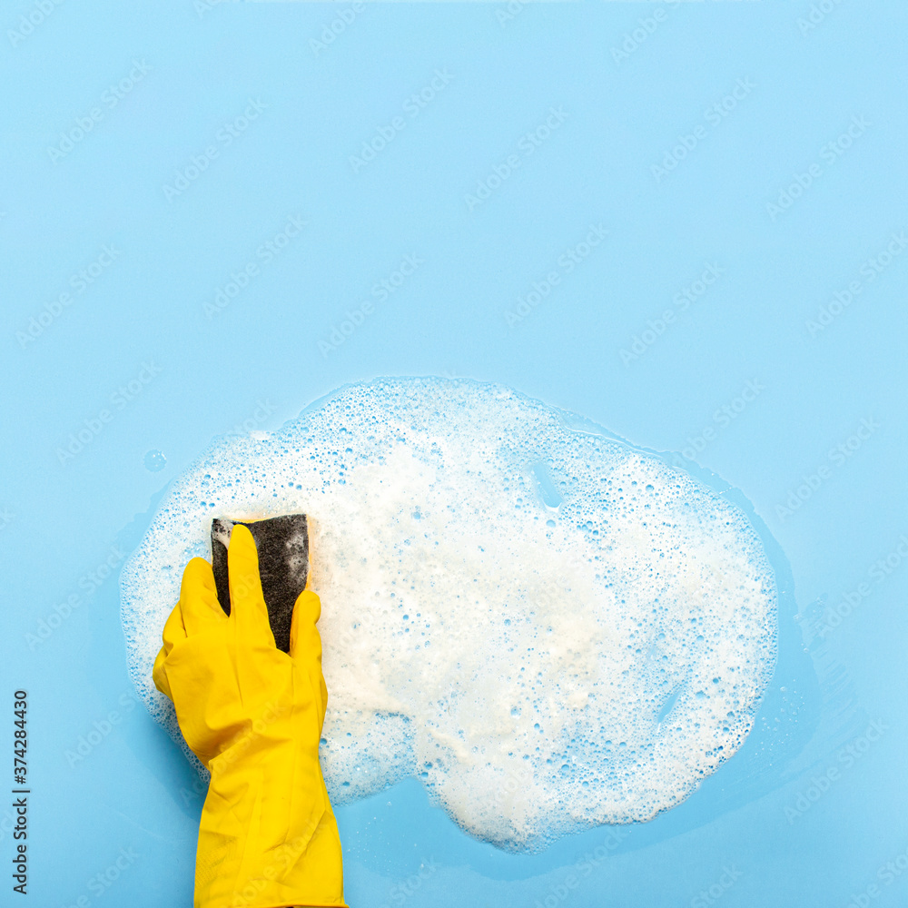 Hand in a yellow rubber glove holds a cleaning sponge and wipes a soapy ...