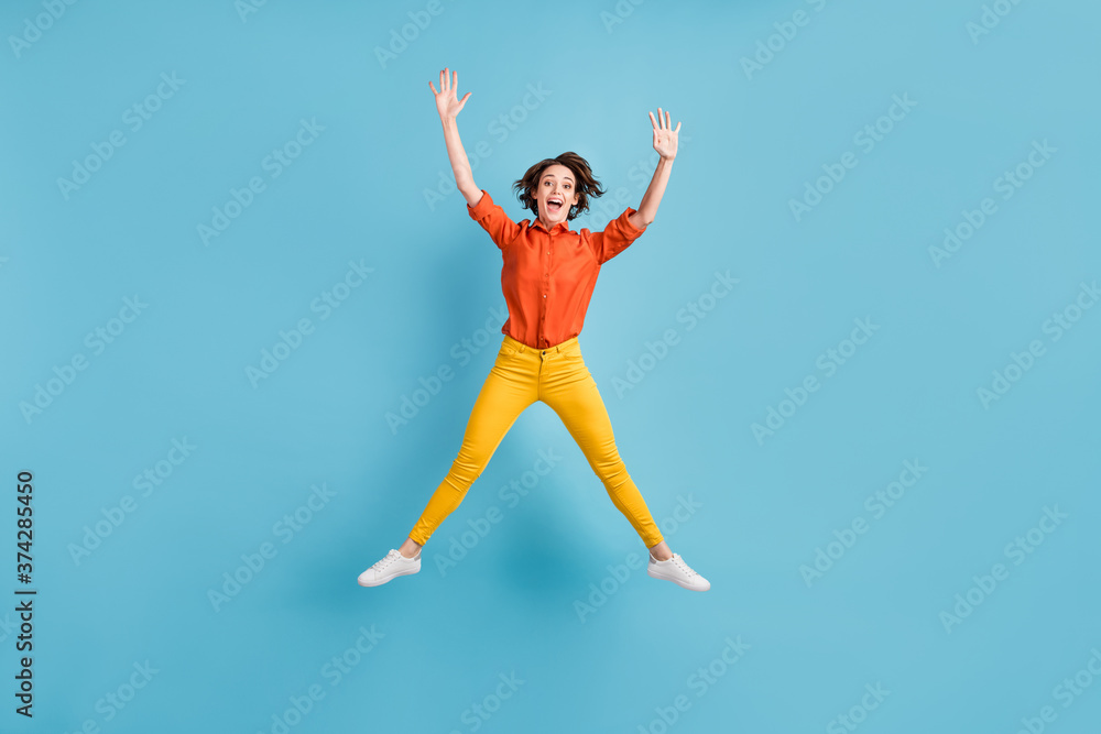 Full length photo of attractive crazy funky lady jump high up positive emotions rejoicing good mood star figure wear orange shirt yellow trousers sneakers isolated blue color background Full length photo of attractive crazy funky lady jump high up positive emotions rejoicing good mood star figure wear orange shirt yellow trousers sneakers isolated blue color background