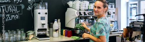 Smiling waitress looking at camera while cleaning coffee maker