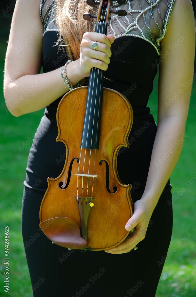 The girl is holding a violin. Brown violin in hands background.