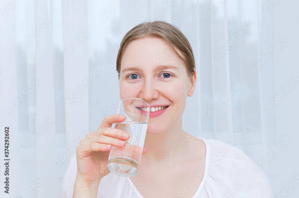 Caucasian blond woman sitting at the table smiling cheerfully holding glass of water in her hands. Caucasian blond woman sitting at the table smiling cheerfully holding glass of water in her hands.