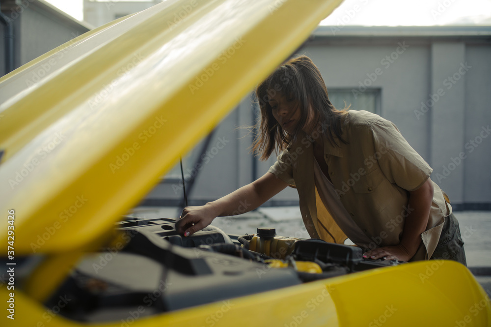 Young woman stands near yellow car with opened bonnet and repairs it. Young woman stands near yellow car with opened bonnet and repairs it.