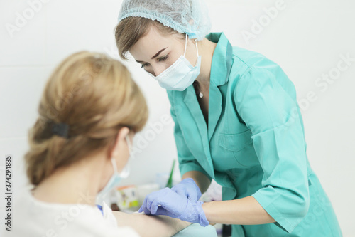 A female nurse in a medical mask takes a blood test from a patient.