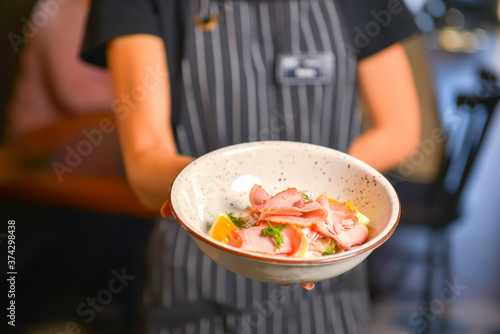 Close up of waiter serving fresh green salad with tomato and ham. Waiter in uniform at work. Restaurant service.