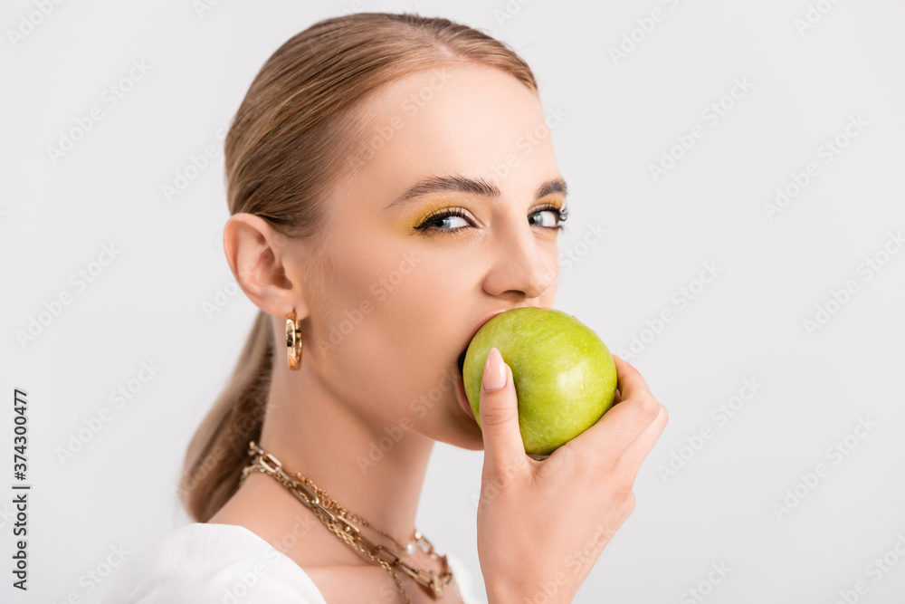 blonde woman biting green apple and looking at camera isolated on white blonde woman biting green apple and looking at camera isolated on white