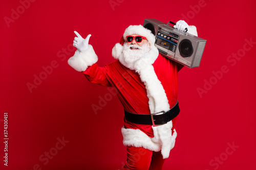 Hip-hop miracle. Full length photo of retired old man grey beard smile hold boombox direct finger empty space wear santa x-mas costume sunglass headwear isolated red color background