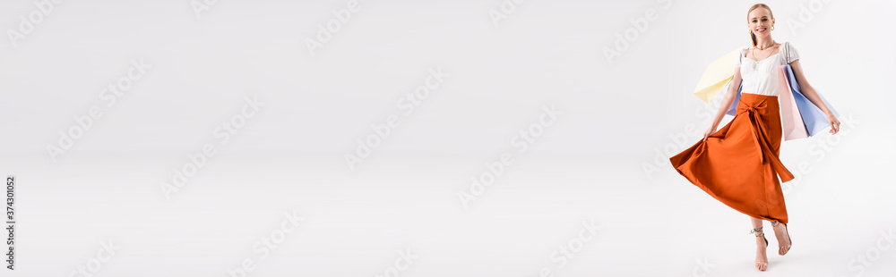 full length view of elegant woman walking with shopping bags on white, panoramic shot