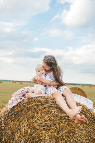Closeup of sister and baby brother kissing on hay bale in wheat field.