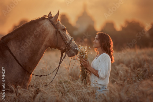Beautiful young woman on spanish buckskin horse in rue field at sunset