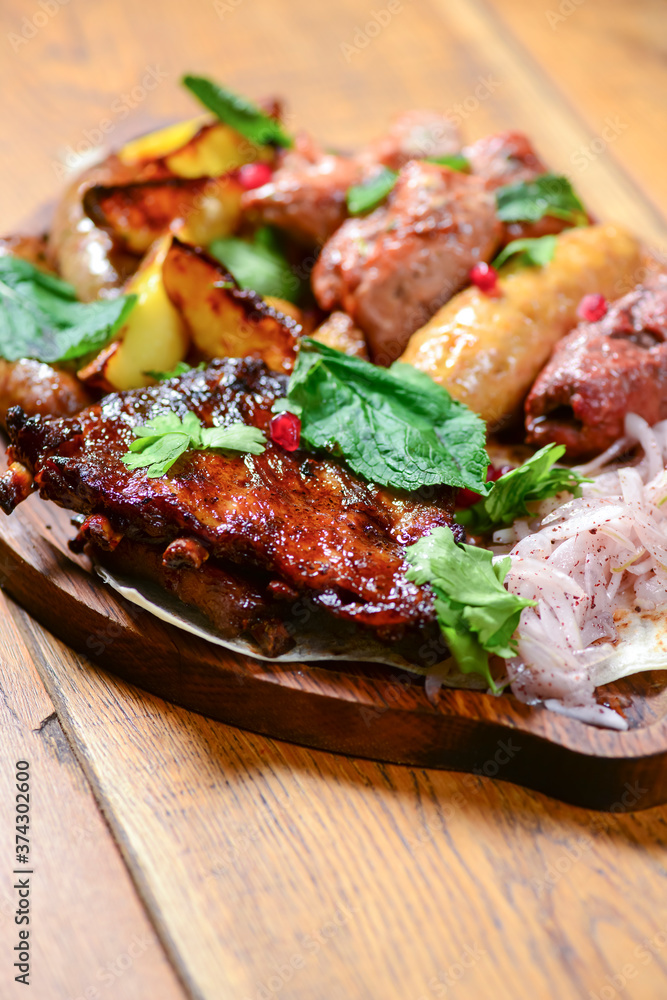 Georgian dinner. Meat, sausages and baked potatoes with fresh greenery served on a wooden board. Georgian dinner. Meat, sausages and baked potatoes with fresh greenery served on a wooden board.