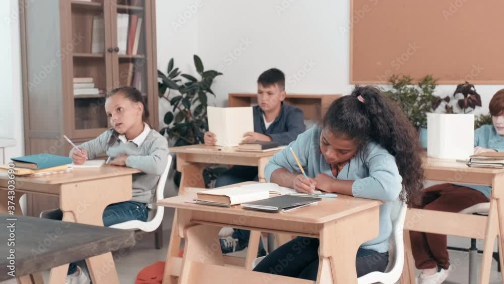 Tracking shot of schoolgirls and schoolboys sitting at desks in classroom and listening to teacher off camera Tracking shot of schoolgirls and schoolboys sitting at desks in classroom and listening to teacher off camera