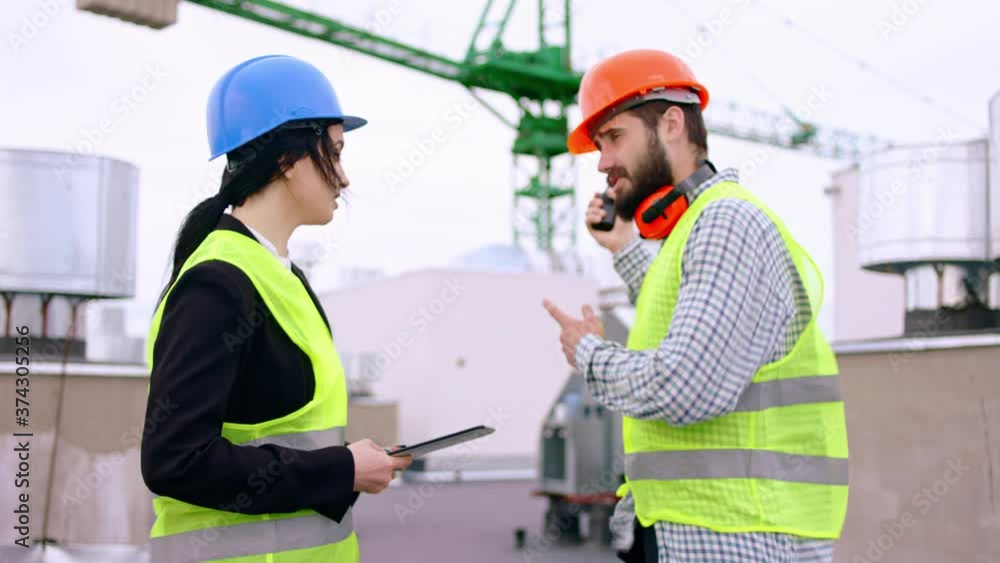 Modern construction site on the top of the building charismatic woman engineer and main builder man with a safety helmets start walking through the construction site analyzing the plan Modern construction site on the top of the building charismatic woman engineer and main builder man with a safety helmets start walking through the construction site analyzing the plan