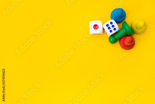 Colorful game chips and two dice are laid out on a yellow background: entertainment, games at home for the whole family, the concept of Board games. Board game. Table games, space for text photo