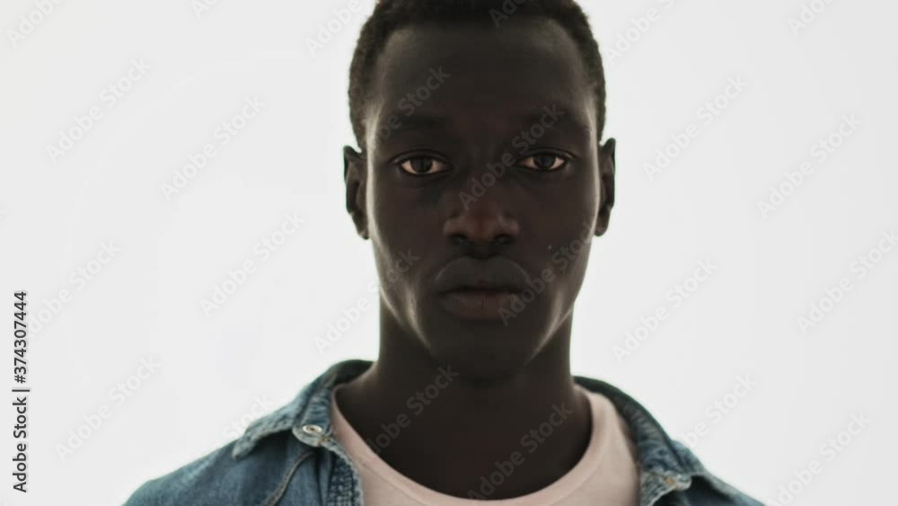 A close-up view of an attractive african american young man is looking to the camera standing isolated over a blue background A close-up view of an attractive african american young man is looking to the camera standing isolated over a blue background