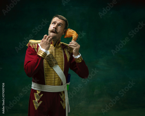 Fast food order. Young man in suit as Nicholas II isolated on dark green background. Retro style, comparison of eras concept. Beautiful male model like historical character, monarch, old-fashioned.