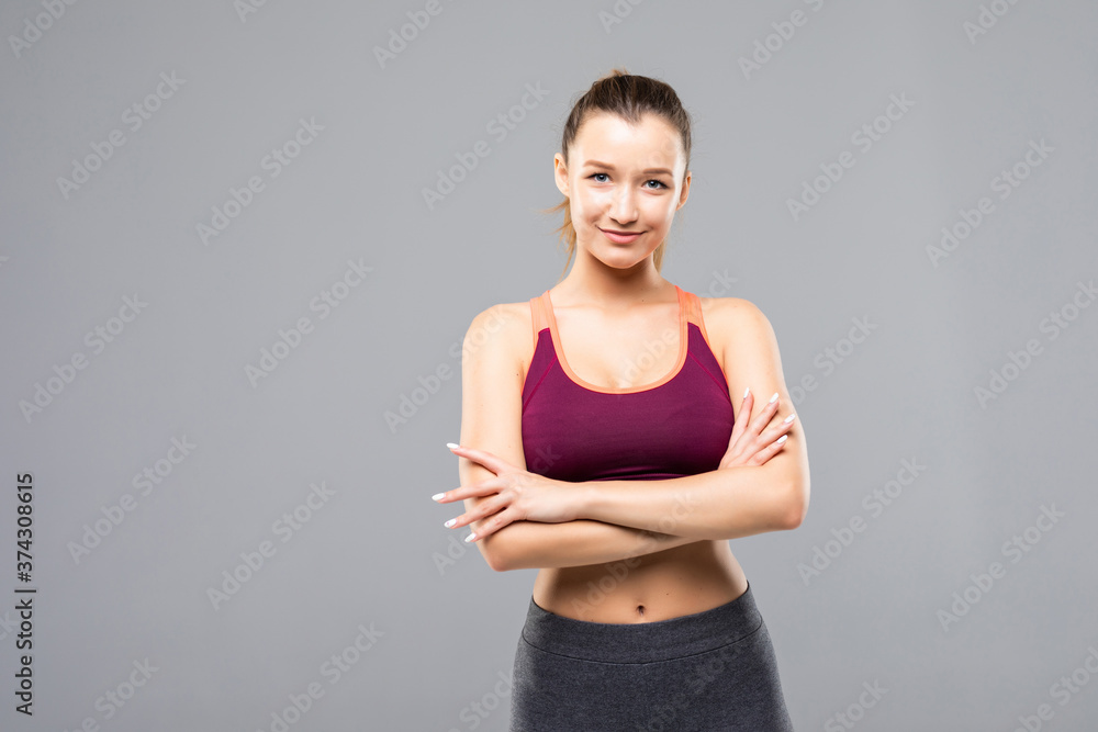 Happy fitness woman standing with arms folded over gray background Happy fitness woman standing with arms folded over gray background