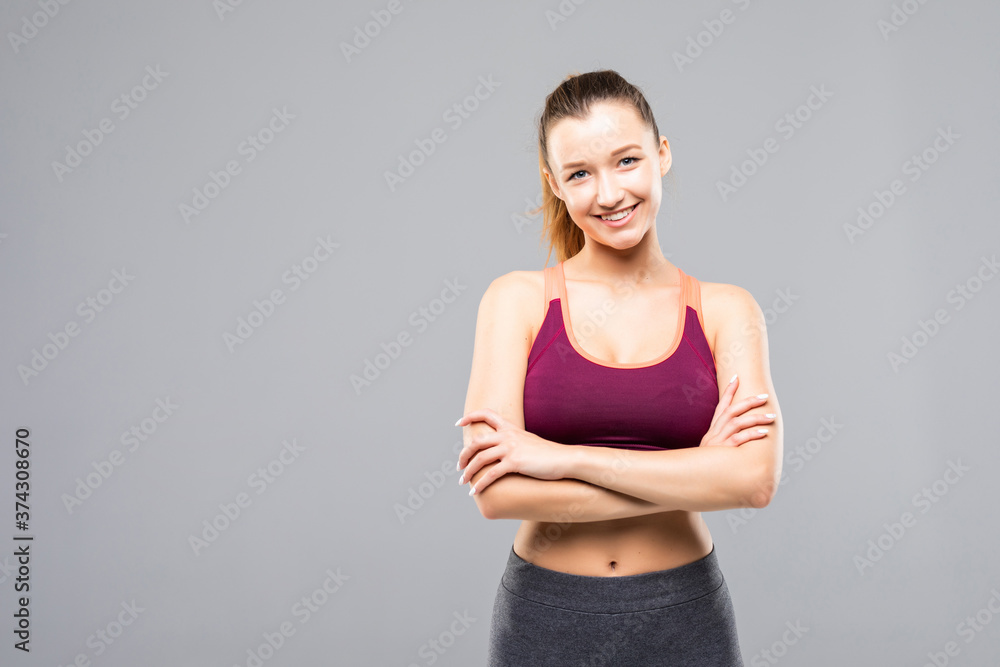 Happy fitness woman standing with arms folded over gray background