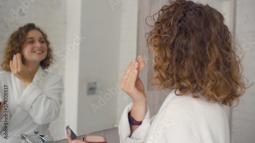 Beautiful young woman applying make-up near mirror in bathroom