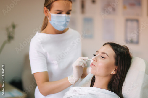 Young woman cosmetologist apply white clay mask on woman's face. Beautiful brunette woman in beauty salon